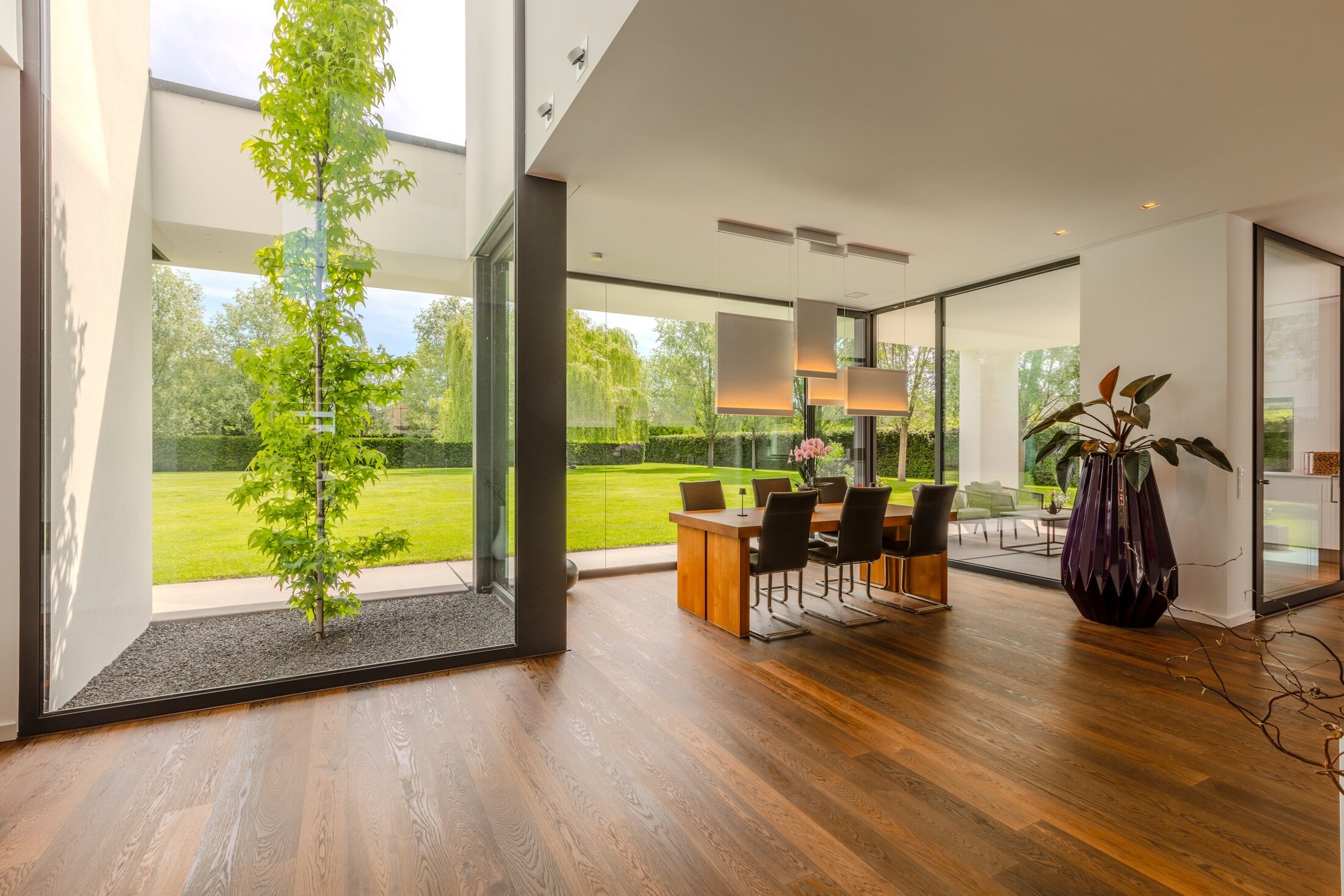 Doppelgeschossiges Atrium mit lebendem Baum, Essbereich und Gartenblick